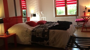 Een slaapkamer met een bed, een bureau, een stoel en een raam met rode luiken.