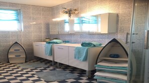 Une salle de bain avec un carrelage à motifs géométriques, un lavabo blanc avec un miroir au-dessus, et des serviettes pliées et rangées sur des étagères.