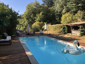 A swimming pool with lounge chairs and umbrellas, surrounded by trees and a wooden deck. - Mas Cévenol typical family, isolated, quiet, private pool in the heart of 20ha (Anduze)