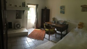 A room with a bed, a desk, a chair, a radiator, a window with curtains, and a wall with a picture. - Mas Cévenol typical family, isolated, quiet, private pool in the heart of 20ha (Anduze)