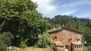 A rustic stone house with red shutters, surrounded by lush greenery and trees. - Mas Cévenol typical family, isolated, quiet, private pool in the heart of 20ha (Anduze)