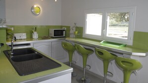 Une cuisine équipée d’un évier, d’un four à micro-ondes et de trois tabourets de bar.