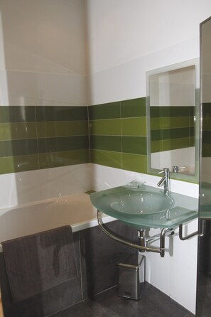 A modern bathroom with a glass sink, a bathtub, and a green-tiled wall. - Holiday farmhouse at the vineyard in the Camargue (Arles)