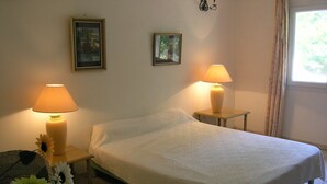 Un lit bien fait, recouvert d’une courtepointe blanche, avec deux lampes de chevet et une chaise en osier recouverte d’un tissu bleu.