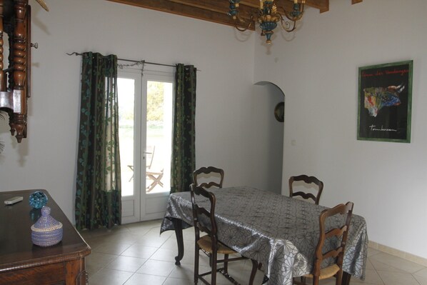 Uma sala de jantar com uma mesa, cadeiras, um candelabro e uma porta com cortinas.