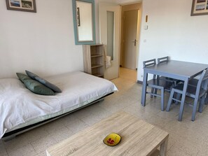 A bedroom with a bed, a small table, a chair, a mirror, and a door leading to a bathroom. - Banyuls-sur-Mer: F2 Apartment with Loggia and Parking, Close to Beach (Banyuls-sur-Mer)