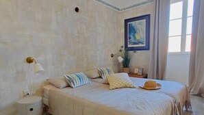 A bedroom with a large bed, bedside lamps, a nightstand, a potted plant, and a painting on the wall. - Casa Delia (L'Île-Rousse)