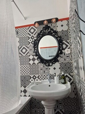 Une salle de bain avec un lavabo blanc, un miroir à cadre noir et des carreaux décoratifs sur les murs.