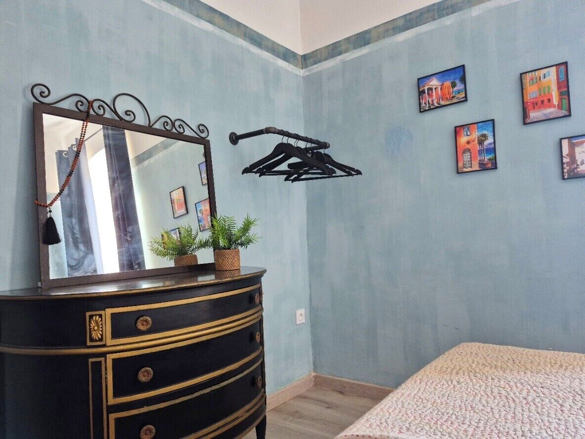 A bedroom with a dresser, a mirror, a hanging clothes rack, and a bed.