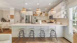 A modern kitchen with a central island, bar stools, pendant lights, and a view of the outdoors.