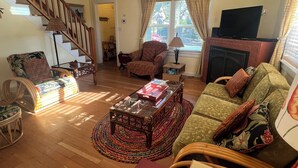 Una sala de estar con una escalera de madera, una chimenea, un televisor y un rincón de descanso acogedor con un sillón y un sofá estampados.