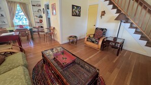 Amplia sala de estar con piso de madera, comedor con mesa verde y escalera con barandas de madera.