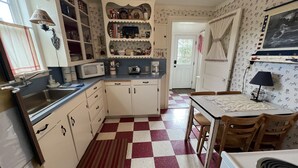 A compact kitchen with white cabinets, a checkered floor, and a dining area with a table and chairs. - Adorable Cottage with Americana Theme, in the Heart of Gearhart. (Seaside)
