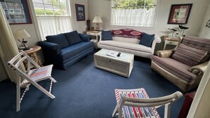 A living room with a blue sofa, a white sofa, a patterned armchair, a coffee table, and a side table with a lamp. - Adorable Cottage with Americana Theme, in the Heart of Gearhart. (Seaside)