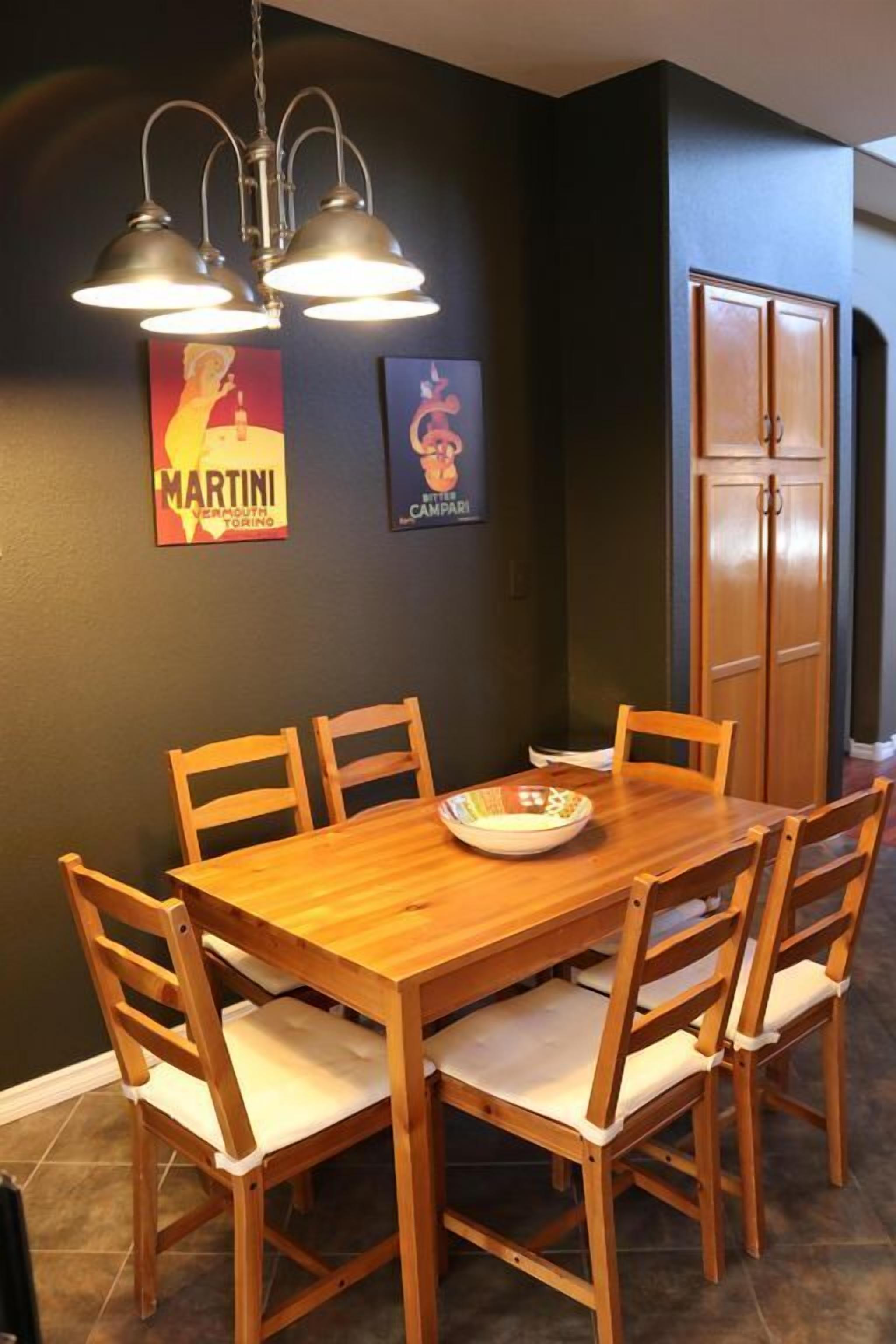 A dining area with a wooden table and chairs, a chandelier, and two framed pictures on the wall.