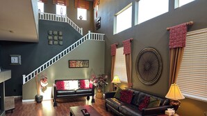 Ein geräumiges Wohnzimmer mit Treppe, einem schwarzen Ledersofa, einem Holztisch und einem großen dekorativen Ventilator.