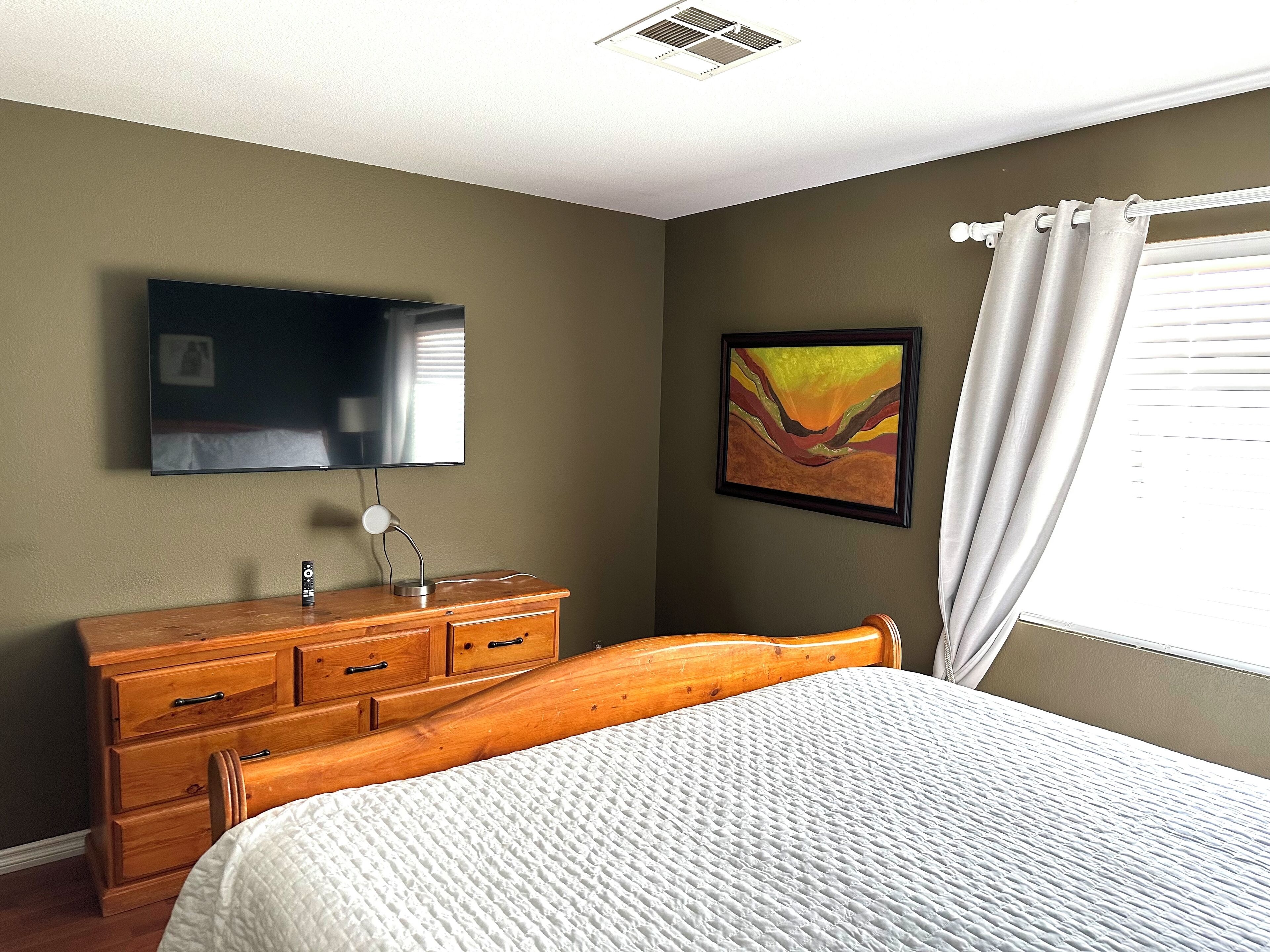 Une chambre à coucher comprenant un lit, une commode, un téléviseur fixé au mur et un tableau.