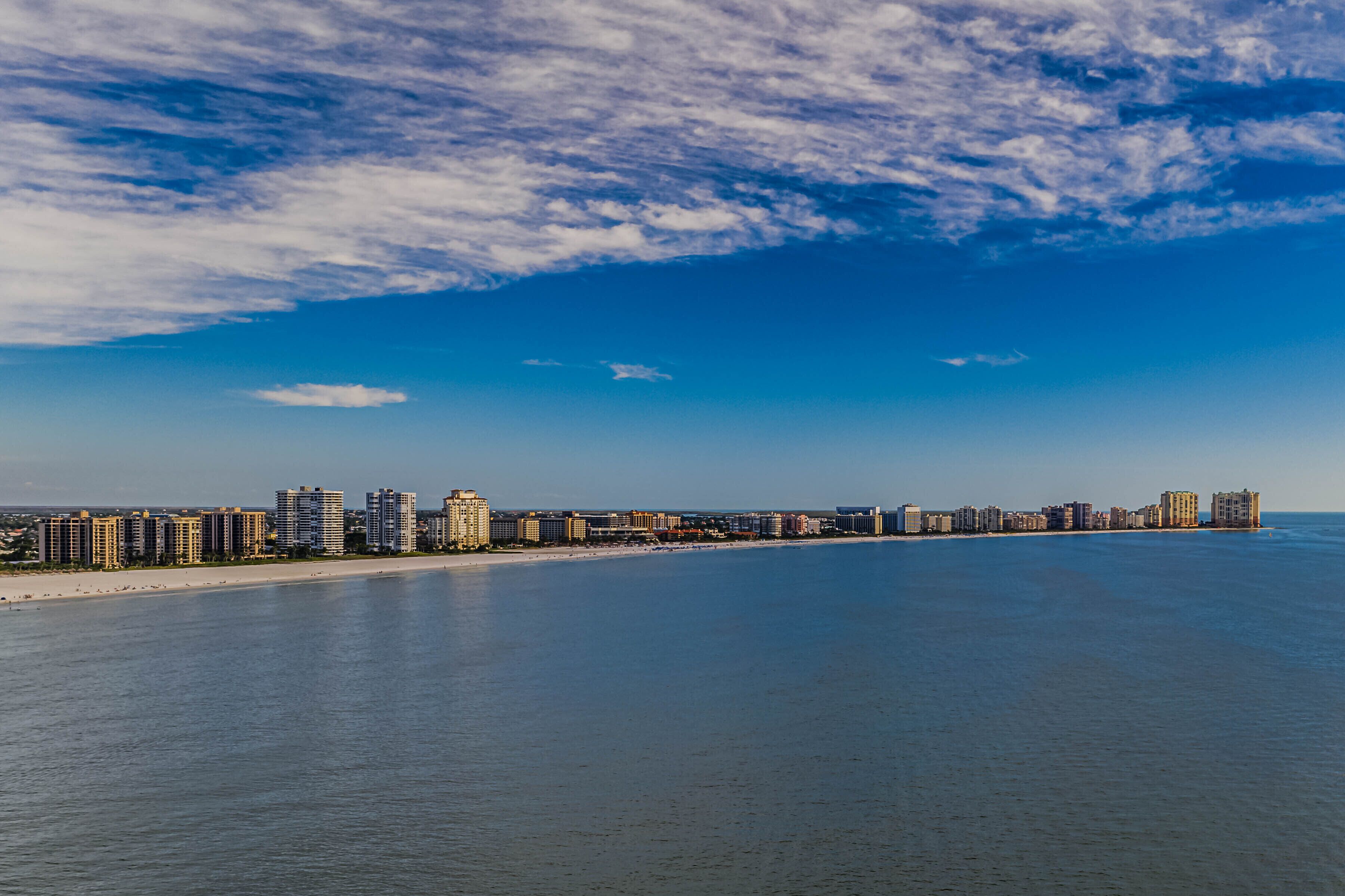 A coastal cityscape with a long beachfront, high-rise buildings, and a clear sky.