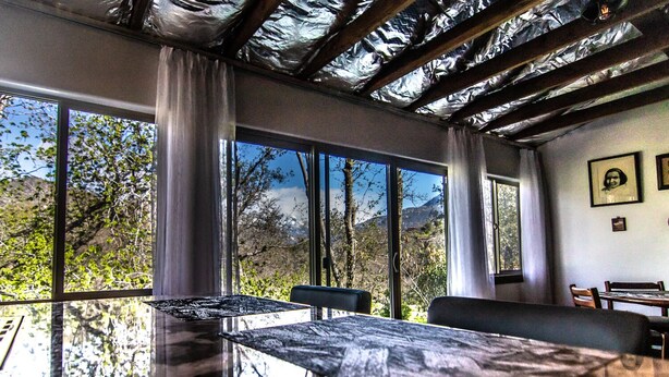 Un comedor con una mesa grande y sillas, ventanas amplias con vista a la montaña y un techo con vigas de madera a la vista.