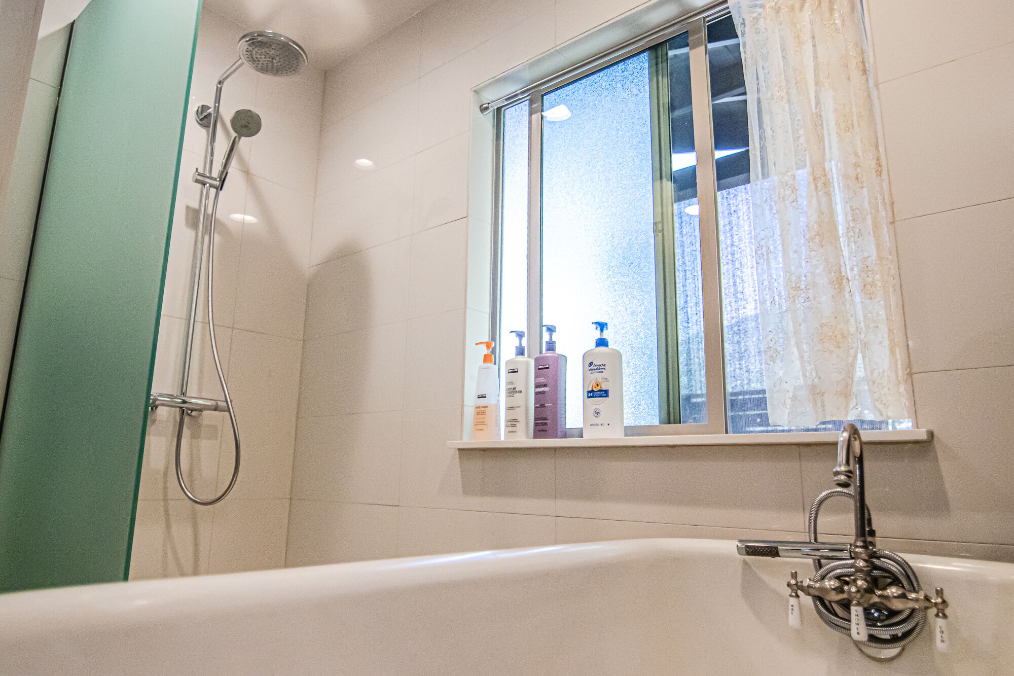 A bathroom with a bathtub, a shower, and a window with toiletries on the sill.