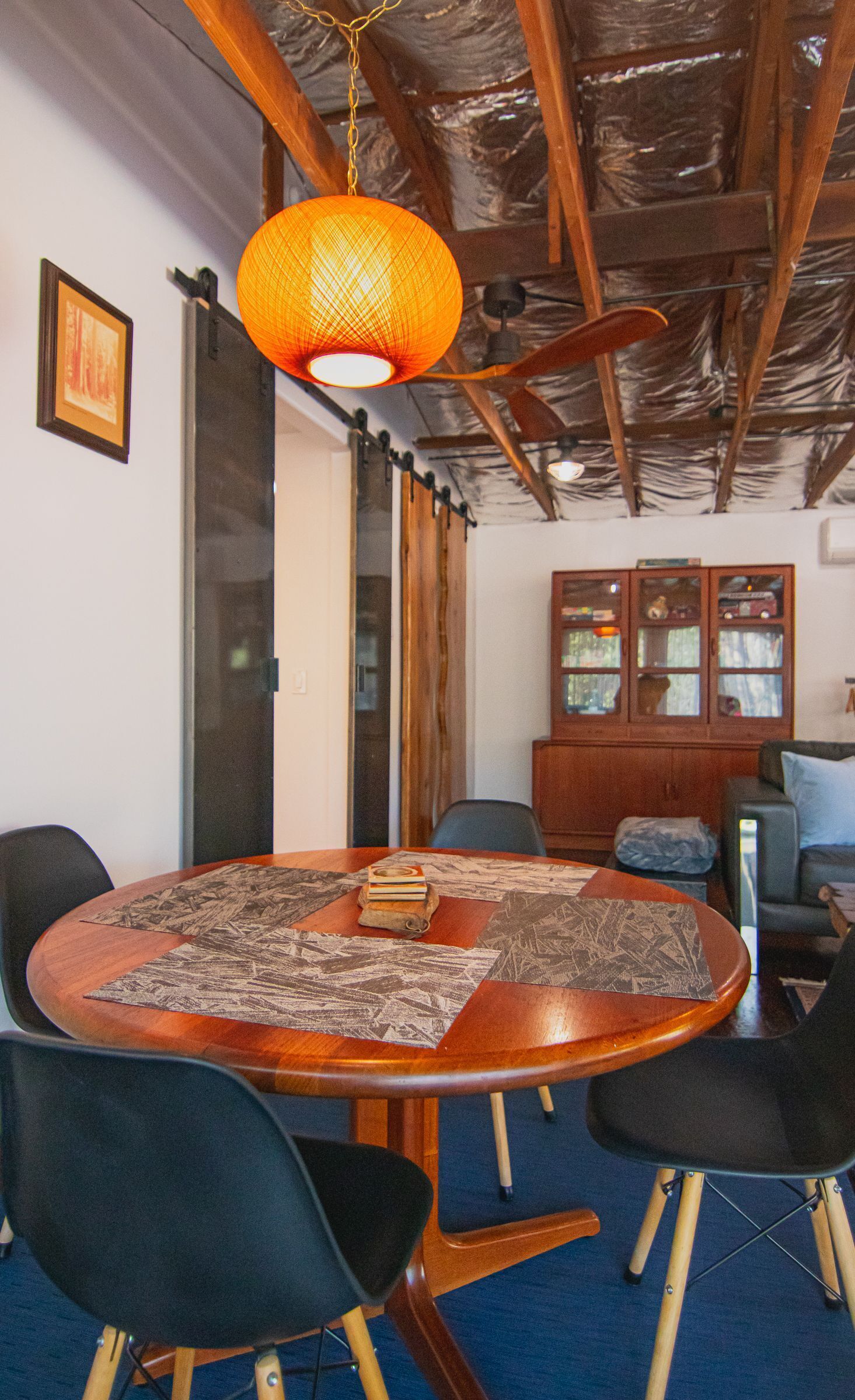 Een vergaderruimte met een houten tafel, zwarte stoelen, een hangende oranje lamp en een houten kast met glazen deuren.