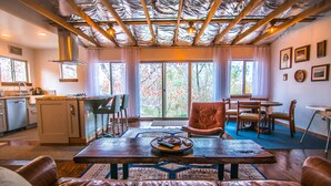 Una sala de estar acogedora con comedor, techo de madera y ventanas amplias con cortinas.