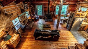 A log cabin interior with a cozy living area, a fireplace, wooden floors, and a dining area.