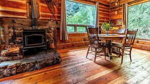 A rustic cabin interior with a stone fireplace, wooden dining table, and chairs.