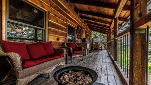 A log cabin with a covered porch, wicker furniture, and a wood-burning stove.