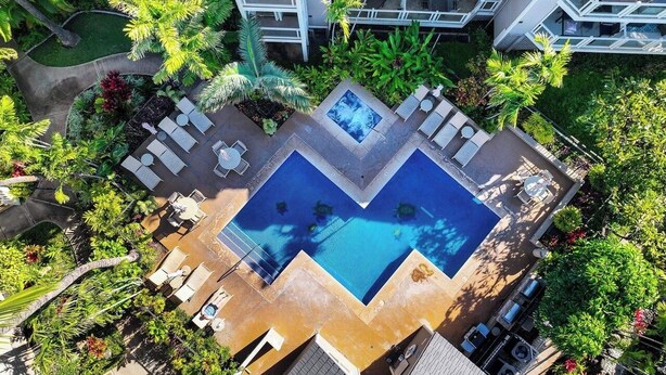 Oversigtsbillede af et hotel med en central swimmingpool, omgivet af loungeområder og frodig vegetation.