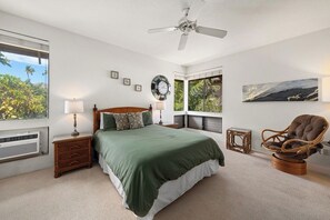 A bedroom with a bed, bedside tables, a chair, a ceiling fan, and a window with a view.