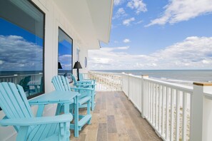 Een balkon met blauwe Adirondack-stoelen, een tafel en een lamp.