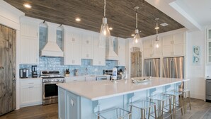 A modern kitchen with white cabinets, stainless steel appliances, and a large island with stools. - "The Pearl" GULF FRONT w/prvt heated pool, 12 bdrm /12.5bath "ALVacationRentals" (Gulf Shores)