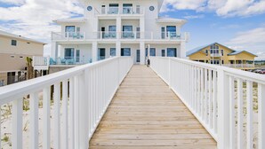 A wooden boardwalk leading to a white multi-story building with balconies, a beach view, and a clear sky. - "The Pearl" GULF FRONT w/prvt heated pool, 12 bdrm /12.5bath "ALVacationRentals" (Gulf Shores)