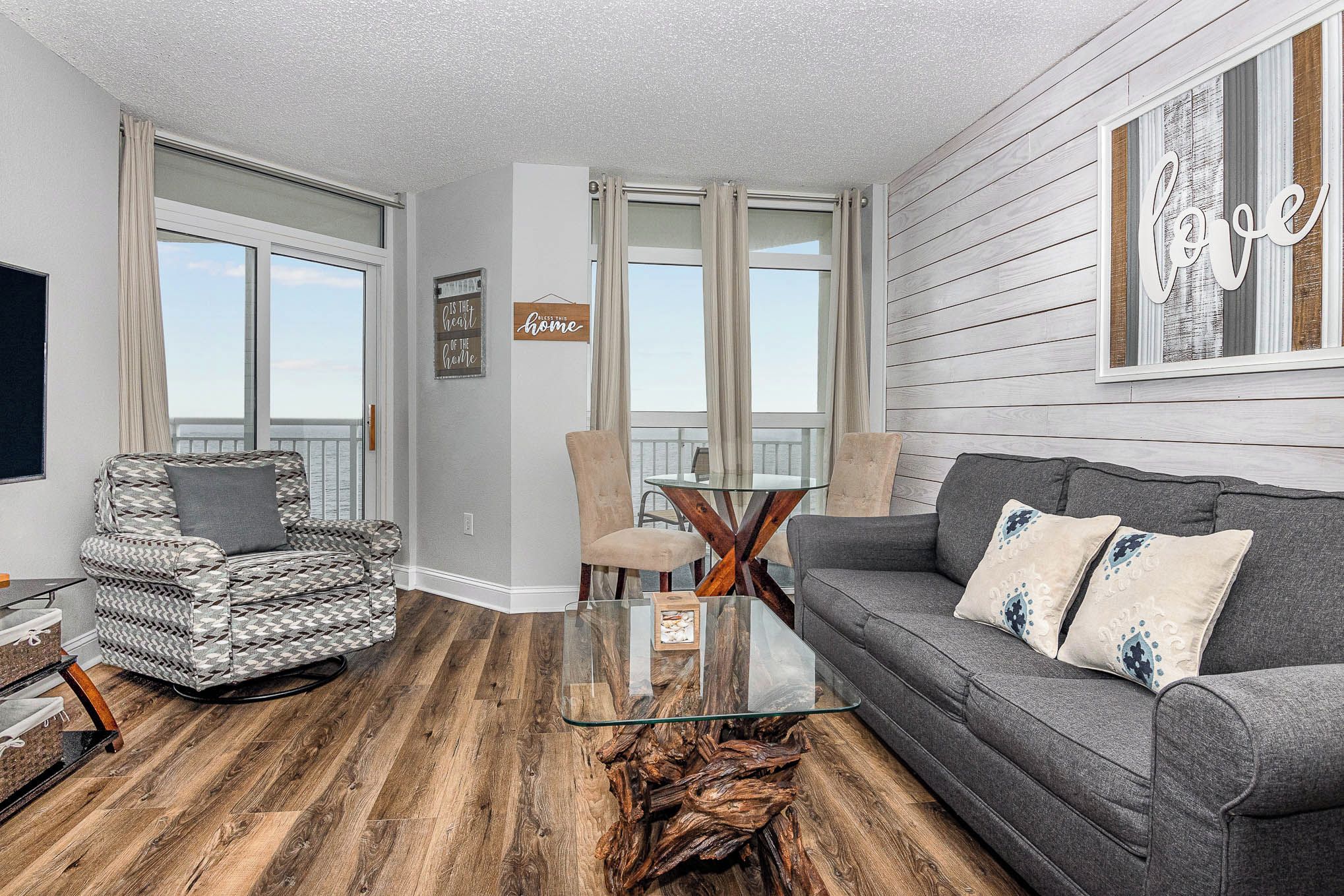 A living room with a grey sofa, a patterned armchair, a glass coffee table, and a wooden side table.