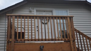 Une terrasse en bois avec une rambarde, une porte et une fenêtre décorée d’une guirlande.