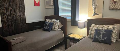 Una habitación con dos camas, una ventana con cortinas, un aire acondicionado instalado en la pared y una decoración con motivos marinos.