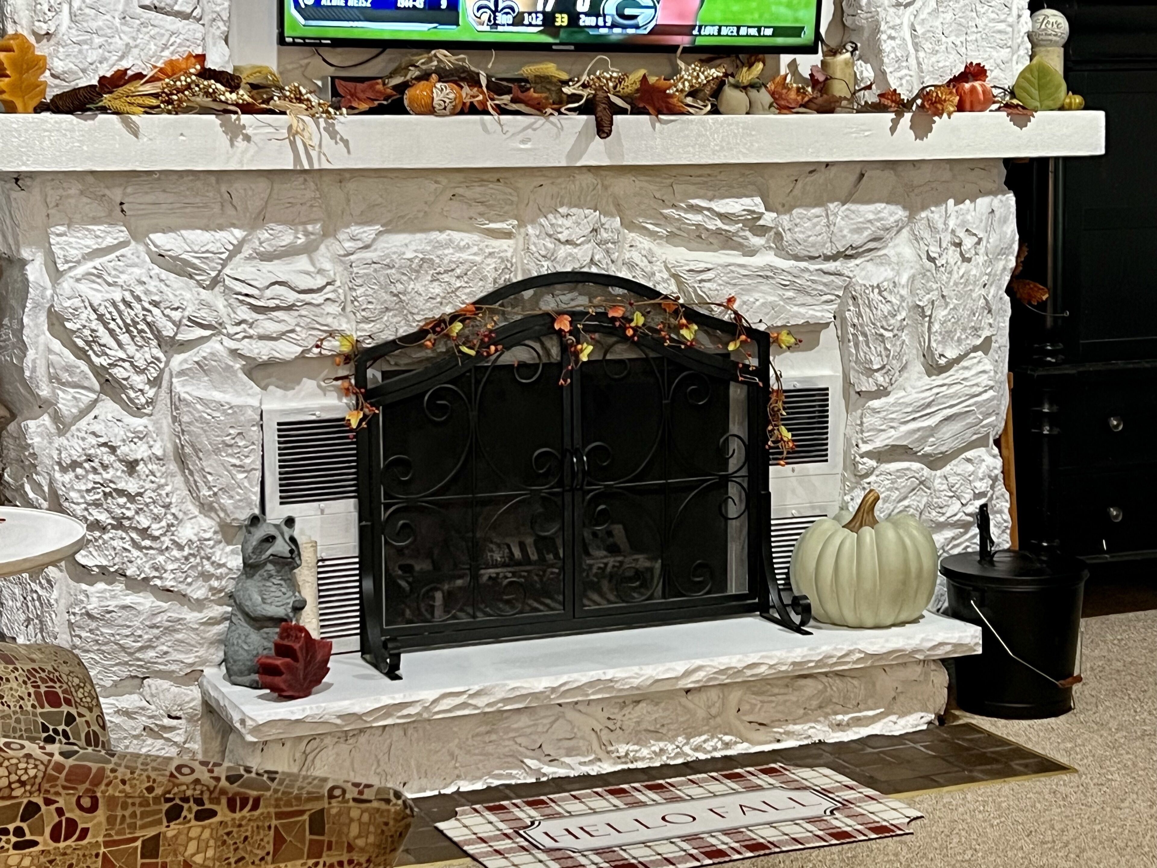 A fireplace with a stone facade, decorative elements, and a 'Hello Fall' mat.