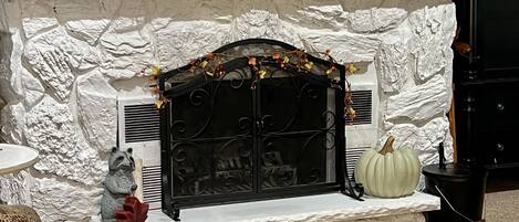 A fireplace with a stone facade, decorative elements, and a 'Hello Fall' mat.