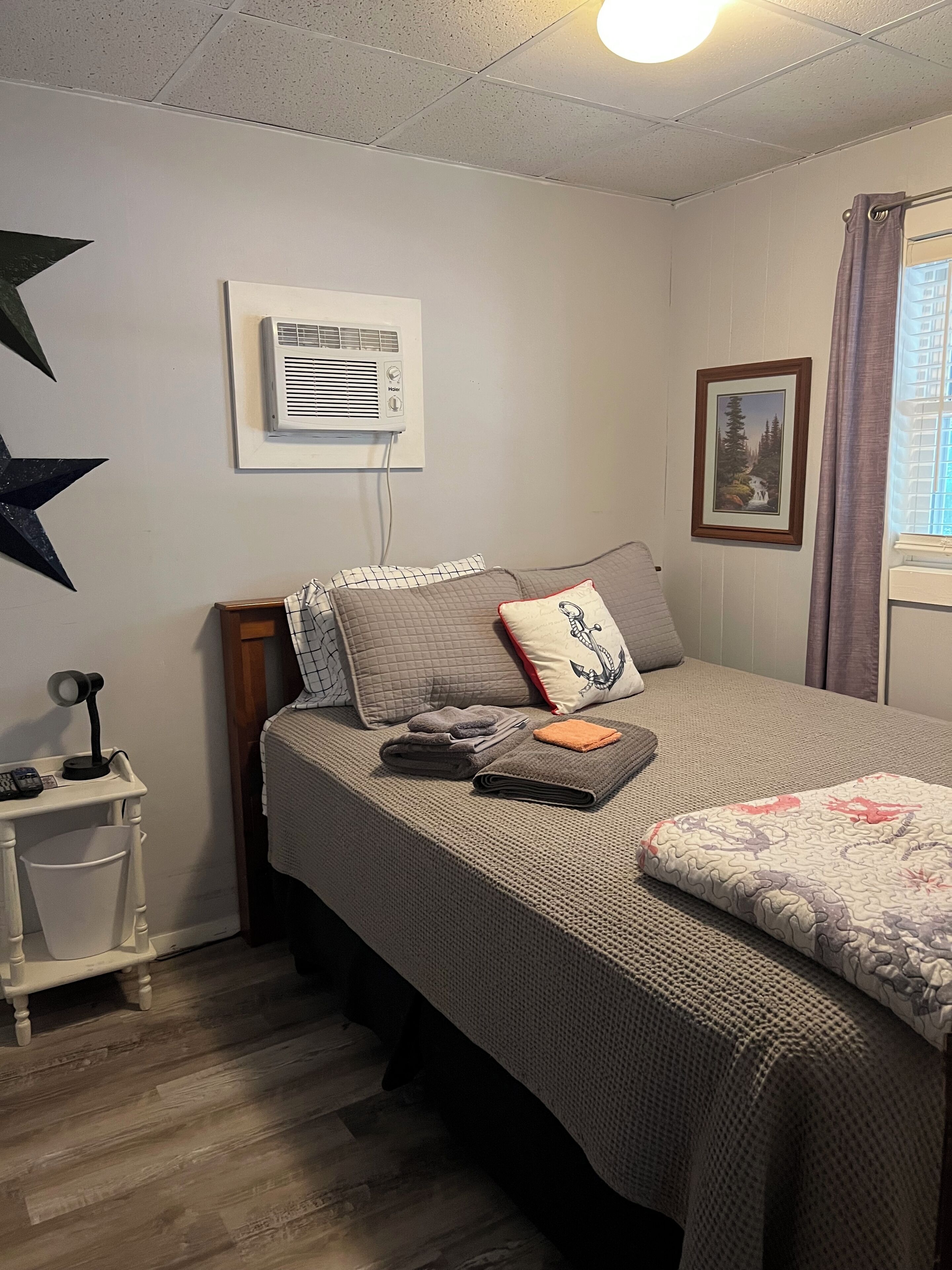 Une chambre bien rangée, avec un lit, une table de chevet et un climatiseur fixé au mur.