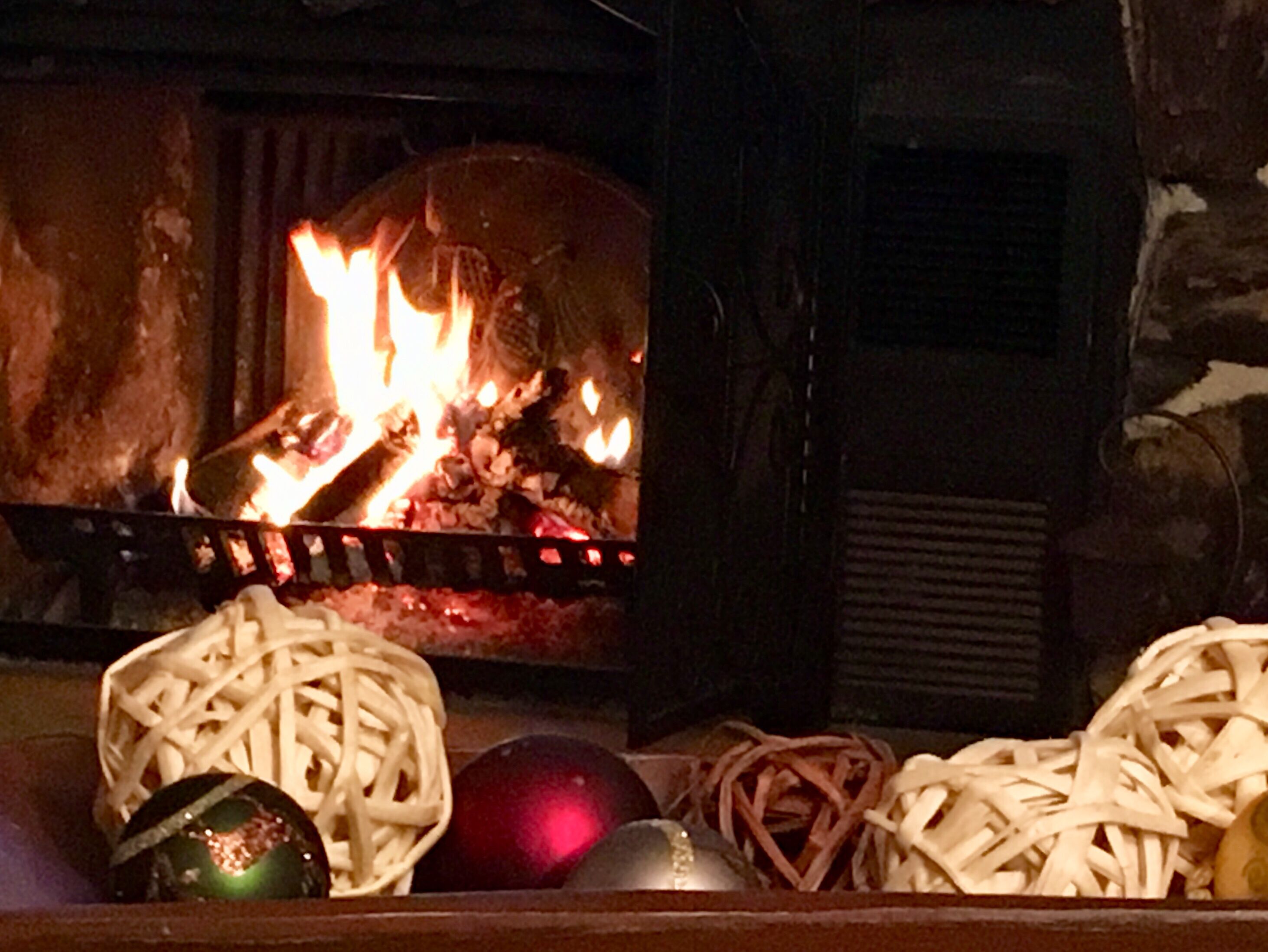 Una chimenea con leña ardiendo, un adorno navideño y una cesta de fideos blancos.