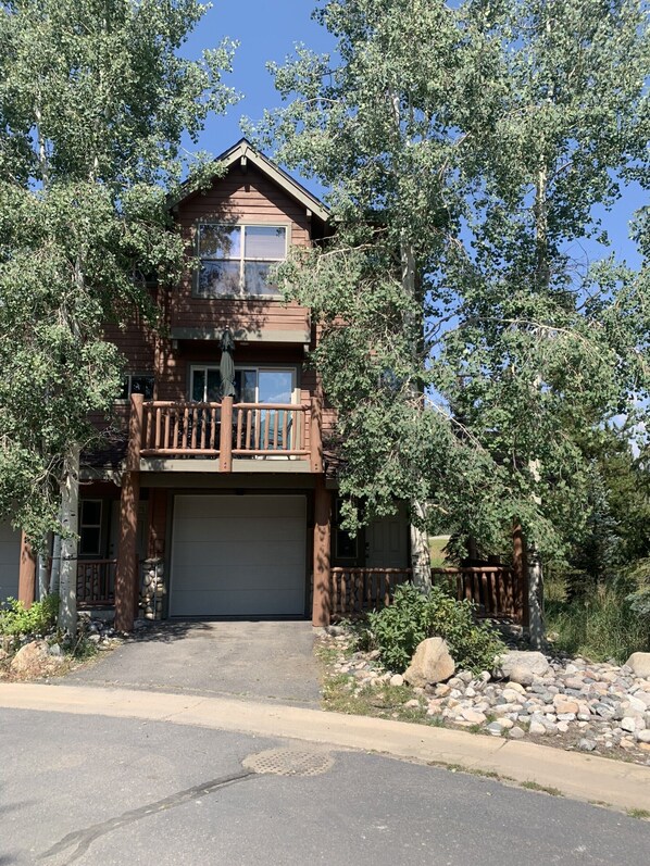 A two-story house with a garage, surrounded by trees and a stone wall.