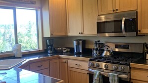 A kitchen with wooden cabinets, a stainless steel stove, a microwave, and a window with a view of trees.