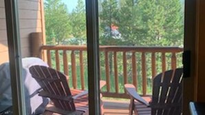 A covered deck with two Adirondack chairs and a table, overlooking a forested area.