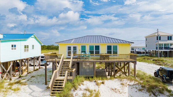 A beach house with a wooden deck and a staircase leading to a balcony.