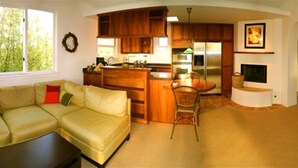 A living room with a beige sectional sofa, a wooden dining table, and a kitchen area with wooden cabinets and a built-in stove. - Charming Casita in Sleepy Beach Community (Encinitas)