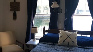 A bedroom with a bed, a chair, a nightstand, a lamp, and a window with curtains.