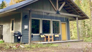 A rustic cabin with a covered porch, large windows, and a picnic table.