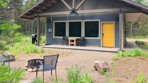 A cabin with a porch, two windows, and a yellow door.