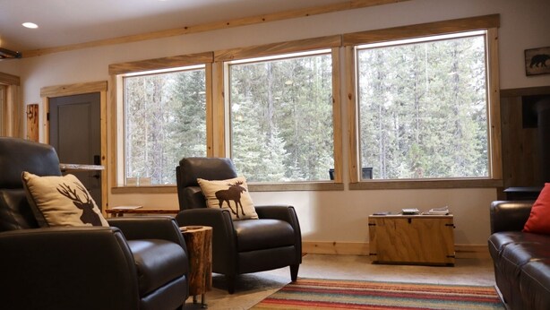 A cozy living room with leather sofas, a wooden coffee table, and large windows offering a forest view.